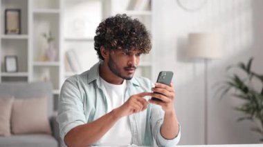 Memnun Hintli adam e-postalarını kontrol ediyor ve iyi haberlerle mutlu. Kazanan genç adam zaferi kutluyor masada oturuyor, ellerini yukarı kaldırıyor.