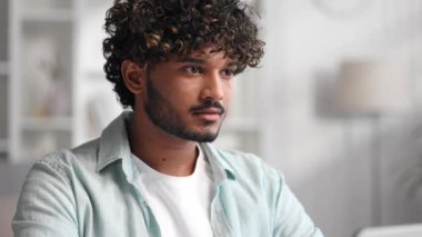 Ofisinde bilgisayar başında çalışan genç Hintli bir adamın portresi, kameraya bakmak için başını çevirir ve samimi bir şekilde gülümser. Kapat.