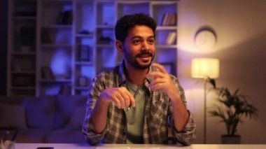 Genç bir Arap akşamleyin oturma odasındaki masada otururken aile dostlarıyla video görüşmesi yapıyor. Kameraya gülümseyen mutlu bir adam, sohbetten memnun. Web kamerasından görüntüle