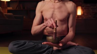 An elderly gray-haired man practices yoga at home using a Tibetan singing bowl for meditation and relaxation