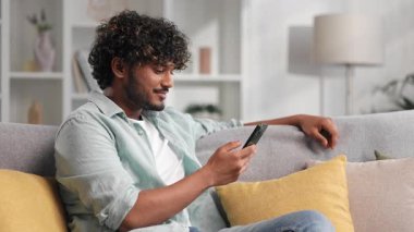 Sakallı ve en sevdiği şarkıyı dinleyen mutlu genç adam. Hintli esmer adam kanepeye oturur ve işten sonra dinlenir. Arkadaşlarına mesaj atmak için akıllı telefonu kullanır. Ekrana tıklatır.