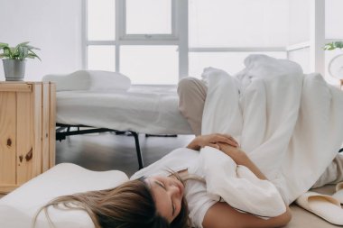 Asyalı Taylandlı kadın, beyaz yataktan düşerken, yerde yatarken, komik pozlar veriyordu..