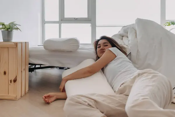 Asian Thai woman falling down from bed, sitting on floor and leaning the bed, lazy relaxing alone in home apartment.
