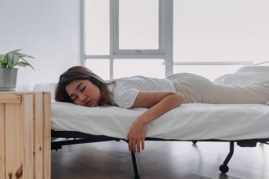 Asyalı Taylandlı kadın yüzüstü yatıyor, beyaz yatakta yatıyor, güzel rüyalar görüyor, sabahları uykulu bir şekilde apartman dairesinde..