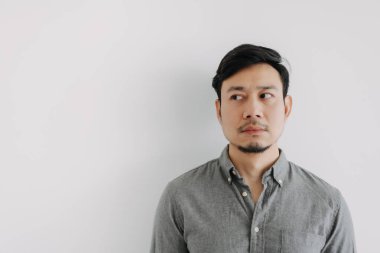 Asyalı sakallı, gri tişörtlü, duygusuz suratlı, beyaz arka plan duvarında izole edilmiş boş bir yere bakan adama yaklaş..