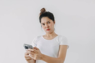 Asyalı Taylandlı kadın, şüpheli bir tavırla cep telefonu kullanıyor, akıllı telefonu tutuyor, beyaz arka plan duvarında tek başına duruyor. Yüksek kalite fotoğraf