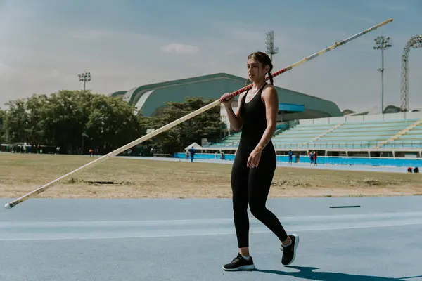 Young athlete woman on athletics track training pole vault