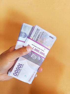 Çok sayıda on bin rupia tutan bir el.