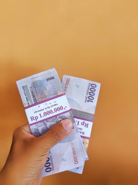 Çok sayıda on bin rupia tutan bir el.