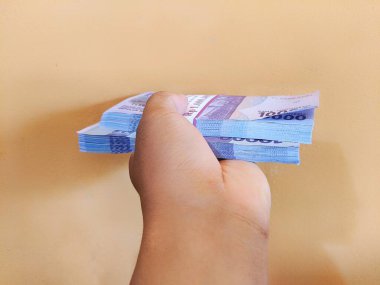 Çok sayıda on bin rupia tutan bir el.