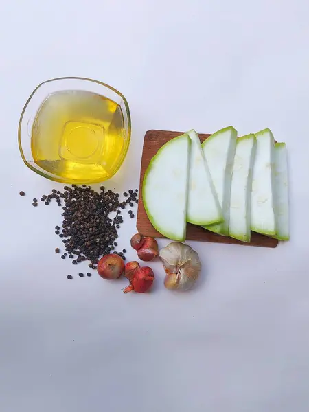 Su kabağı meyvesi parçalanmış, yenilebilir yağ, siyah marika, arpacık soğanı ve sarımsak beyaz arka planda.