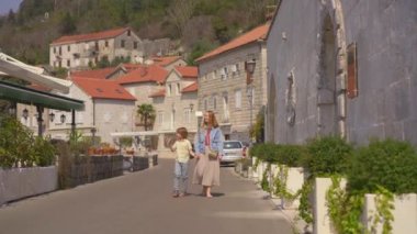 Genç bir kadın ve küçük oğlu Boka-Kotorska körfezindeki Perast şehrinin güzel bir sahil şehrinde yürüyorlar..