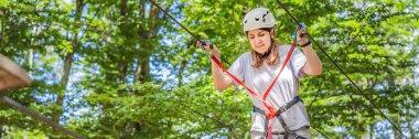 BANNER, BANNER, LONG FORMAT Mutlu kadın kız uçsuz bucaksız yol tramvaylarında tırmanıyor ağaçtaki karabina emniyet halatıyla ağaç tepesindeki halat macera parkına. Aile hafta sonu çocukları.