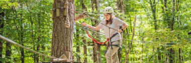 BANNER, BANNER, LONG FORMAT Mutlu kadın kız uçsuz bucaksız yol tramvaylarında tırmanıyor ağaçtaki karabina emniyet halatıyla ağaç tepesindeki halat macera parkına. Aile hafta sonu çocukları.