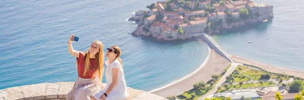 バンナー ロングフォーマットセントスティーブン島の美しい景色を背景に2人の女性観光客 ブドヴァリビエラのスヴェティ シュテファン ブドヴァ モンテネグロ モンテネグロのコンセプトへの旅行 — ストック写真