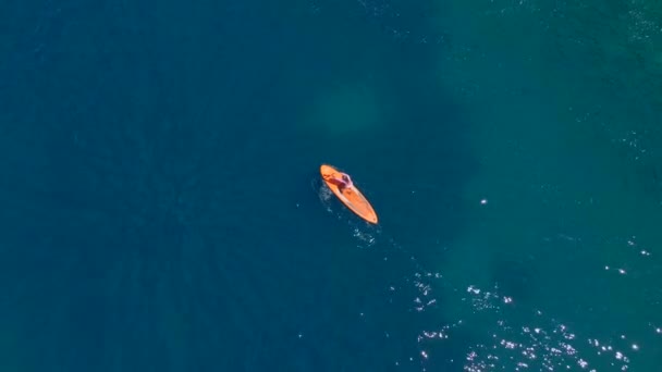 年轻的女人站在站着的船桨板上 Sup在汹涌澎湃的岩石中摇曳着 清澈的蓝色海水环绕着她 空中慢动作视频 — 图库视频影像