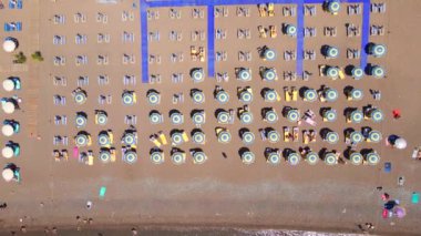 Havadan yavaş çekim videosu. Yukarıdan temiz mavi suyu olan güzel bir kumsalın manzarası. Sahilde çiğ kumsal şemsiyeleri. Yaz mevsimi konsepti.