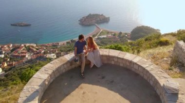 Genç çift, erkek ve kadın Budva kenti yakınlarındaki Sveti Stefan adasının üzerindeki Saint Sava kilisesini ziyaret ediyor. Karadağ 'a Seyahat