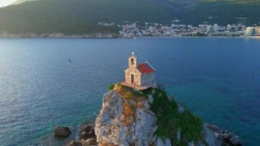 Yavaş çekim hava görüntüsü. Sveta Nedelja - Petrovac şehrine yakın küçük bir adadaki Hristiyan kilisesi Adanın üzerinde bir sürü kukla uçar.