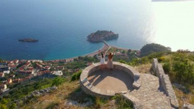 Budva kenti yakınlarındaki Sveti Stefan adasının üzerindeki Saint Sava kilisesini iki kadın ziyaret ediyor. Karadağ 'a seyahat. Yavaş çekim videosu.