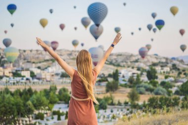 Kapadokya, Türkiye 'de sıcak hava balonlarına bakan turist kadın. İyi yolculuklar hindi konsepti. Dağın tepesinde harika manzaranın tadını çıkaran bir kadın.