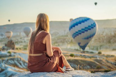 Kapadokya, Türkiye 'de sıcak hava balonlarına bakan turist kadın. İyi yolculuklar hindi konsepti. Dağın tepesinde harika manzaranın tadını çıkaran bir kadın.