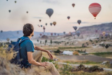 Kapadokya, Türkiye 'de sıcak hava balonlarına bakan bir turist. İyi yolculuklar hindi konsepti. Dağın tepesindeki adam Harika manzaranın tadını çıkarıyor.
