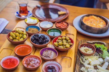 Türk kahvaltı masası. Hamur işleri. Sebzeler. Zeytin. Peynir, yağda yumurta. Reçel, bakır demlikte çay ve lale bardakları. Geniş bileşim.