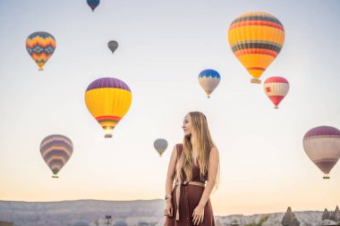 Kapadokya, Türkiye 'de sıcak hava balonlarına bakan turist kadın. İyi yolculuklar hindi konsepti. Dağın tepesinde harika manzaranın tadını çıkaran bir kadın.