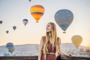 Kapadokya, Türkiye 'de sıcak hava balonlarına bakan turist kadın. İyi yolculuklar hindi konsepti. Dağın tepesinde harika manzaranın tadını çıkaran bir kadın.