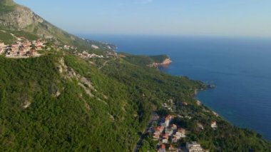 Hava videosu. İnsansız hava aracı Karadağ kıyı şeridi boyunca Budva kenti ve Sveti Stefan adasına yakın uçuyor. Adriyatik Denizi manzaralı pitoresk bir köy.