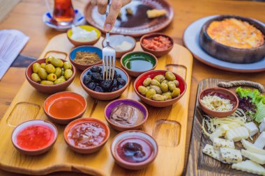 Türk kahvaltı masası. Hamur işleri. Sebzeler. Zeytin. Peynir, yağda yumurta. Reçel, bakır demlikte çay ve lale bardakları. Geniş bileşim.