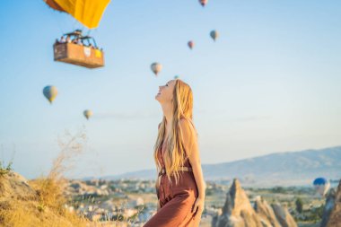 Kapadokya, Türkiye 'de sıcak hava balonlarına bakan turist kadın. İyi yolculuklar hindi konsepti. Dağın tepesinde harika manzaranın tadını çıkaran bir kadın.