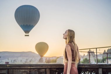Kapadokya, Türkiye 'de sıcak hava balonlarına bakan turist kadın. İyi yolculuklar hindi konsepti. Dağın tepesinde harika manzaranın tadını çıkaran bir kadın.