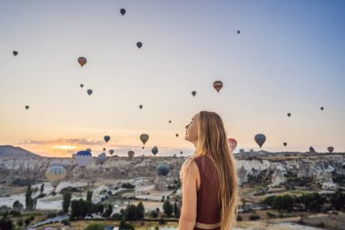 Kapadokya, Türkiye 'de sıcak hava balonlarına bakan turist kadın. İyi yolculuklar hindi konsepti. Dağın tepesinde harika manzaranın tadını çıkaran bir kadın.