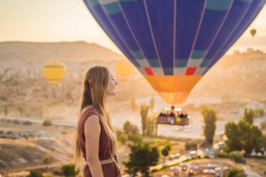 Kapadokya, Türkiye 'de sıcak hava balonlarına bakan turist kadın. İyi yolculuklar hindi konsepti. Dağın tepesinde harika manzaranın tadını çıkaran bir kadın.
