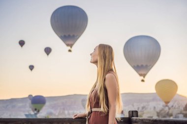 Kapadokya, Türkiye 'de sıcak hava balonlarına bakan turist kadın. İyi yolculuklar hindi konsepti. Dağın tepesinde harika manzaranın tadını çıkaran bir kadın.