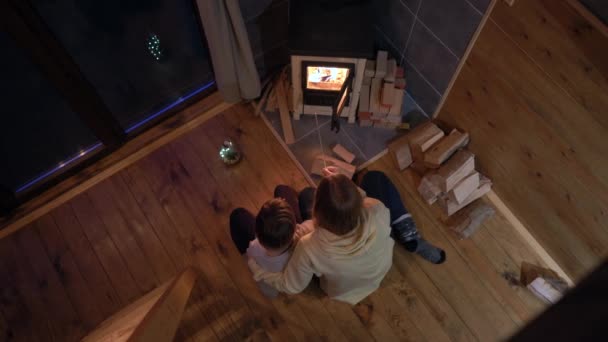 年轻的妇女和她的小儿子坐在一个家庭火炉边看着火 这是个小木屋寒假概念 — 图库视频影像