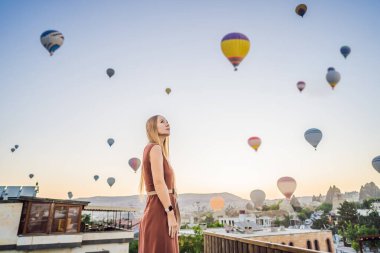 Kapadokya, Türkiye 'de sıcak hava balonlarına bakan turist kadın. İyi yolculuklar hindi konsepti. Dağın tepesinde harika manzaranın tadını çıkaran bir kadın.