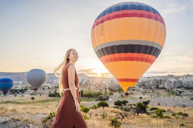 Kapadokya, Türkiye 'de sıcak hava balonlarına bakan turist kadın. İyi yolculuklar hindi konsepti. Dağın tepesinde harika manzaranın tadını çıkaran bir kadın.