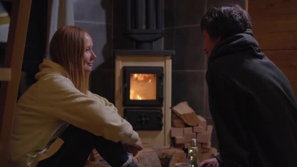 年轻的男女坐在家庭炉边喝茶和谈话 这是个小木屋寒假概念 — 图库视频影像