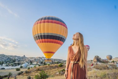 Kapadokya, Türkiye 'de sıcak hava balonlarına bakan turist kadın. İyi yolculuklar hindi konsepti. Dağın tepesinde harika manzaranın tadını çıkaran bir kadın.