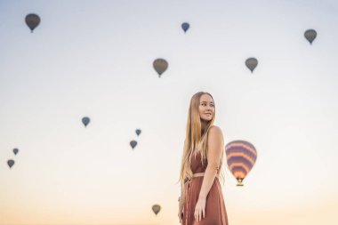 Kapadokya, Türkiye 'de sıcak hava balonlarına bakan turist kadın. İyi yolculuklar hindi konsepti. Dağın tepesinde harika manzaranın tadını çıkaran bir kadın.