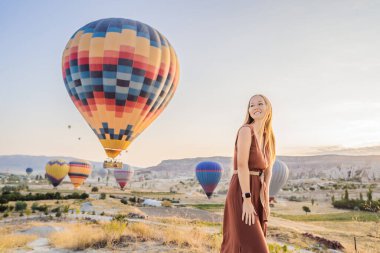 Kapadokya, Türkiye 'de sıcak hava balonlarına bakan turist kadın. İyi yolculuklar hindi konsepti. Dağın tepesinde harika manzaranın tadını çıkaran bir kadın.
