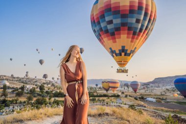 Kapadokya, Türkiye 'de sıcak hava balonlarına bakan turist kadın. İyi yolculuklar hindi konsepti. Dağın tepesinde harika manzaranın tadını çıkaran bir kadın.