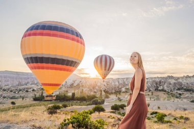 Kapadokya, Türkiye 'de sıcak hava balonlarına bakan turist kadın. İyi yolculuklar hindi konsepti. Dağın tepesinde harika manzaranın tadını çıkaran bir kadın.