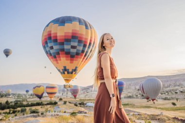Kapadokya, Türkiye 'de sıcak hava balonlarına bakan turist kadın. İyi yolculuklar hindi konsepti. Dağın tepesinde harika manzaranın tadını çıkaran bir kadın.