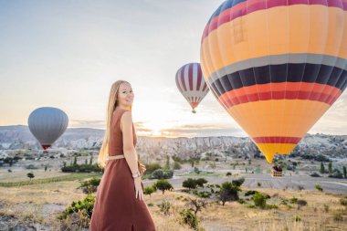 Kapadokya, Türkiye 'de sıcak hava balonlarına bakan turist kadın. İyi yolculuklar hindi konsepti. Dağın tepesinde harika manzaranın tadını çıkaran bir kadın.