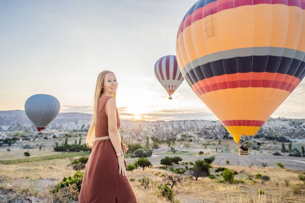 Kapadokya, Türkiye 'de sıcak hava balonlarına bakan turist kadın. İyi yolculuklar hindi konsepti. Dağın tepesinde harika manzaranın tadını çıkaran bir kadın.