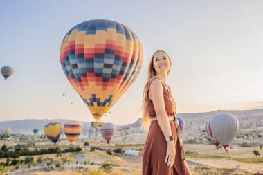 Kapadokya, Türkiye 'de sıcak hava balonlarına bakan turist kadın. İyi yolculuklar hindi konsepti. Dağın tepesinde harika manzaranın tadını çıkaran bir kadın.